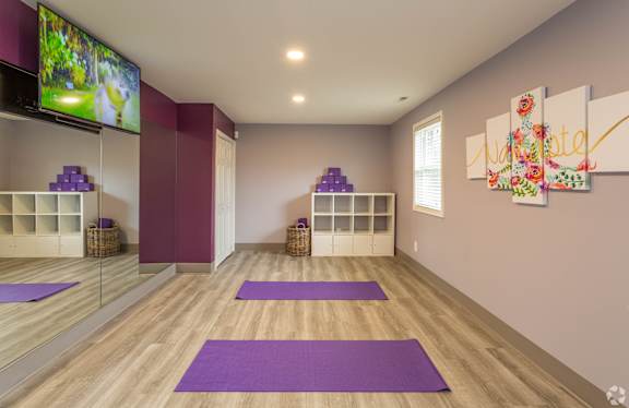 A yoga studio with purple mats and a flat screen TV mounted on the wall.