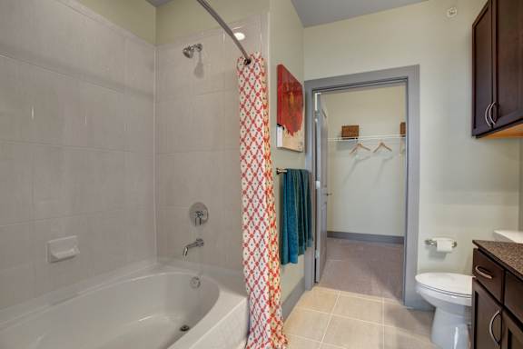 A bathroom with a white tub and a shower curtain with a red and white pattern.