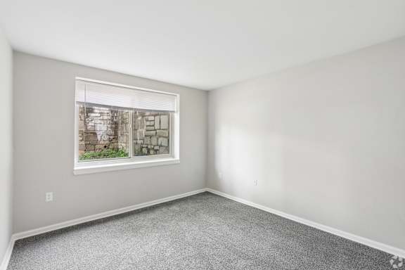 A room with a window showing a view of a stone wall and greenery outside.