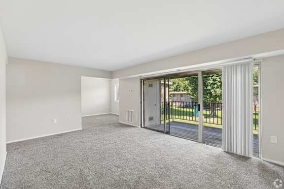 A spacious room with a sliding glass door leading to a balcony.