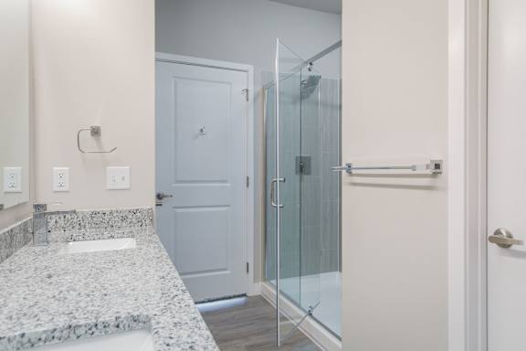 A bathroom with a marble counter top and a glass shower door.