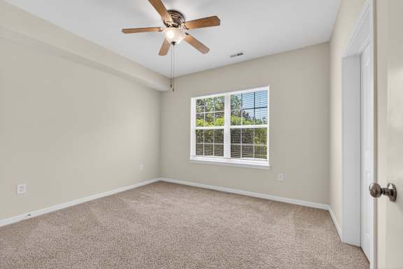 A room with a ceiling fan and a window with a view of trees.