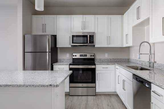 A kitchen with a refrigerator, microwave, oven, and sink.
