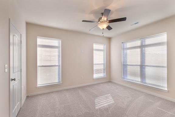 A room with a ceiling fan and three windows.