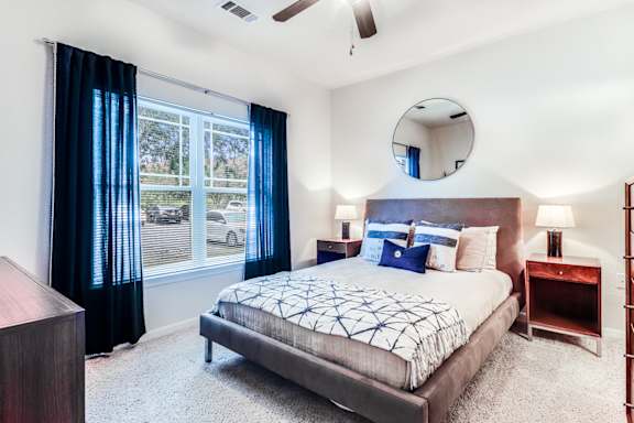 A bedroom with a bed, nightstand, and window with curtains.