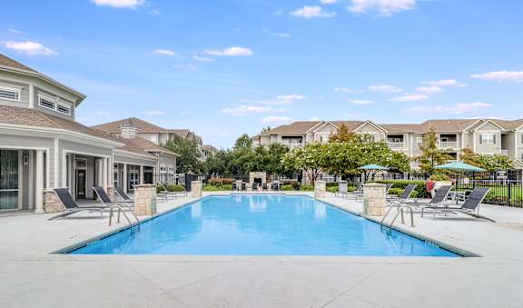 A large swimming pool surrounded by lounge chairs and umbrellas in a residential area.