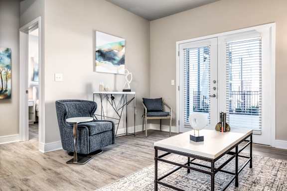 A living room with a grey armchair, a white table, and a painting on the wall.