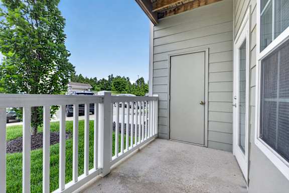 A white fence on a patio with a grey house and a tree in the background.