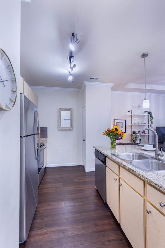 A kitchen with a refrigerator, sink, and wooden floors.