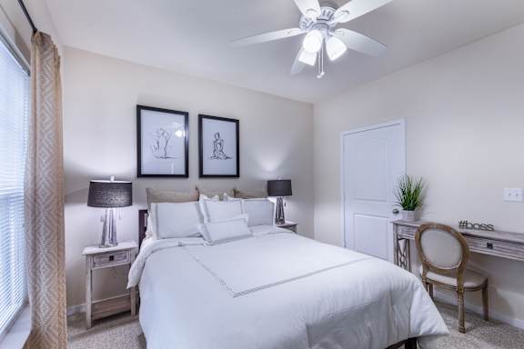 A bedroom with a large bed, a desk with a chair, and two framed pictures on the wall.