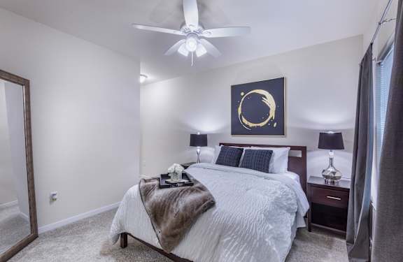 A bedroom with a large bed, a ceiling fan, and a painting on the wall.