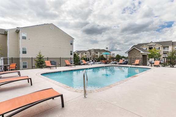 A pool with a slide and sun loungers in front of apartment buildings.