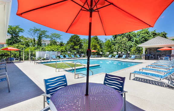 A red umbrella is over a round table with blue chairs.