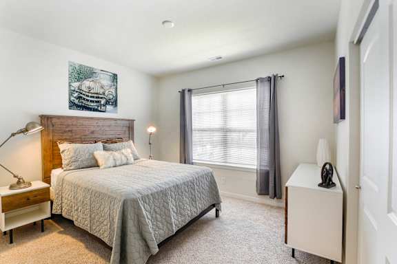 A bedroom with a bed, nightstand, and window.
