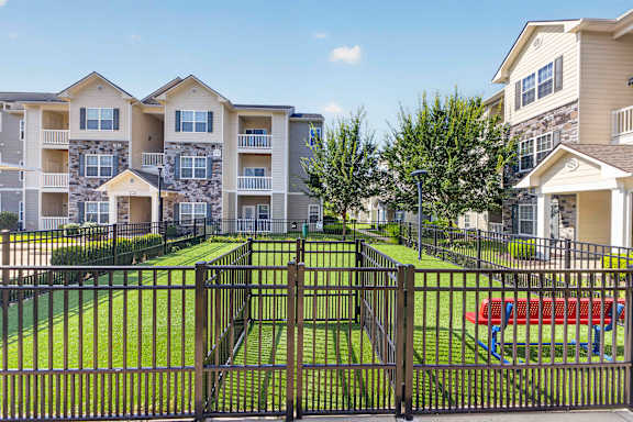 A black metal fence surrounds a green lawn in front of apartment buildings.