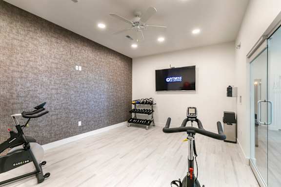 A room with a wall of treadmills and a TV showing a fitness program.