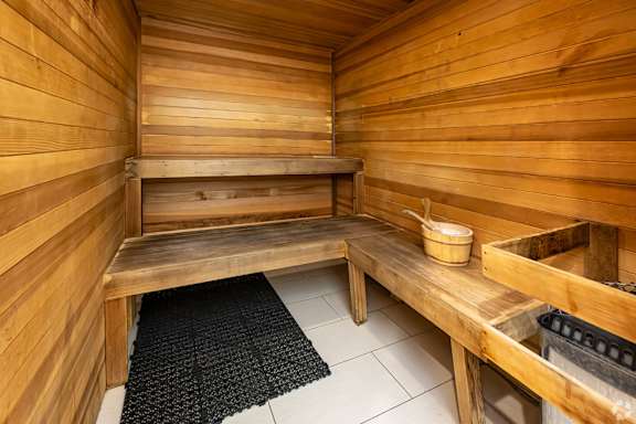 A wooden sauna with a bench and bucket on the table.