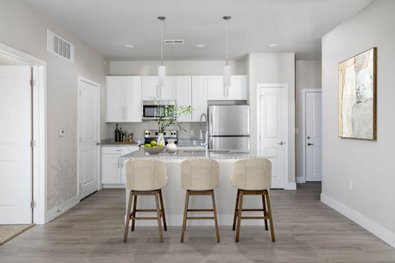 A kitchen with white cabinets and a center island with two chairs.