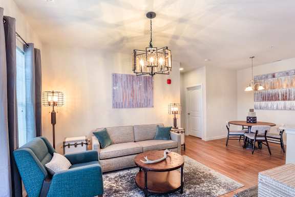 A living room with a grey couch, a blue chair, a wooden coffee table and a chandelier.