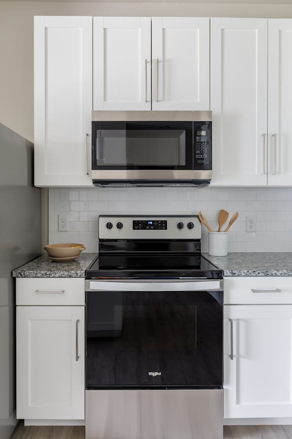 A black microwave is on top of a stove with a bowl on the counter.