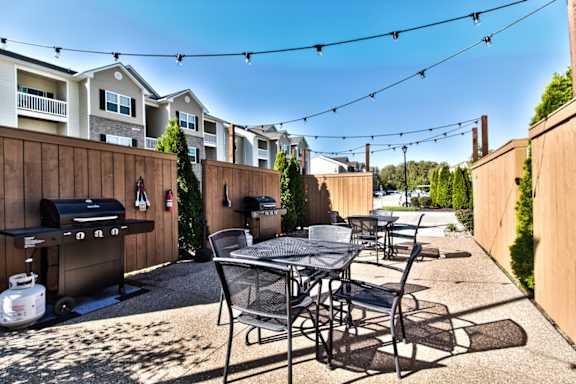 A patio with a grill and chairs is surrounded by a wooden fence.