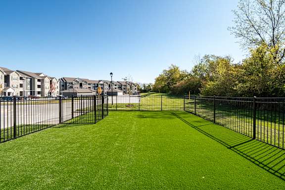 A black fence surrounds a green lawn in front of apartment buildings.