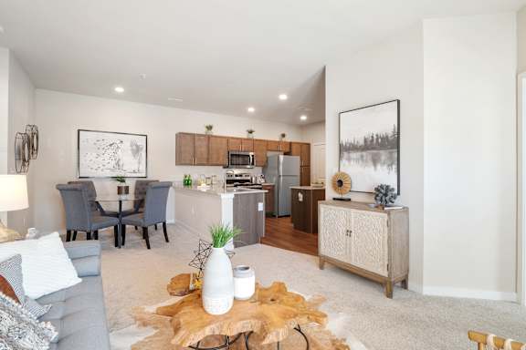 A modern living room with a grey couch, a wooden coffee table, and a kitchen area in the background.