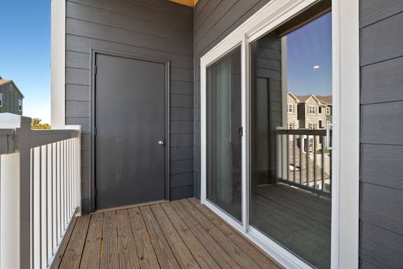 A balcony with a black door and a glass door leading to a deck.