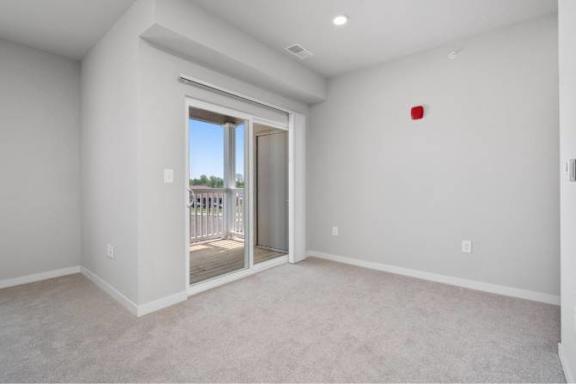 A room with a carpeted floor and a sliding glass door leading to a balcony at Aventura at Wentzville I & II Apartments, Wentzville, MO