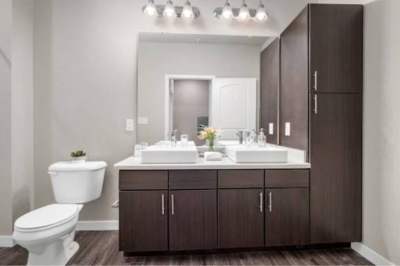 A bathroom with a white toilet, a white sink, and brown cabinets at Aventura at Wentzville I &amp; II Apartments, Missouri