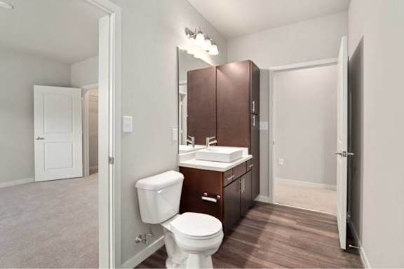 A white toilet sits in a bathroom with brown wood floors and white walls at Aventura at Wentzville I &amp; II Apartments, Wentzville