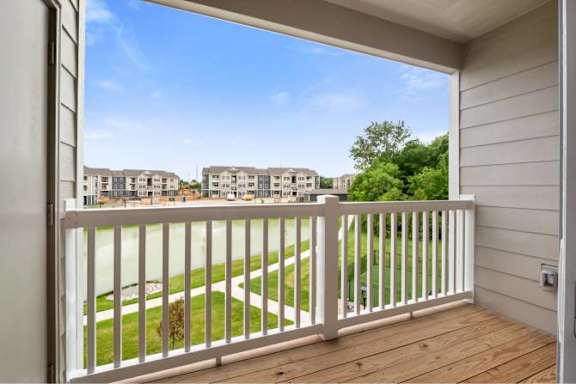 A balcony with a white railing overlooks a grassy area and buildings at Aventura at Wentzville I &amp; II Apartments, Missouri