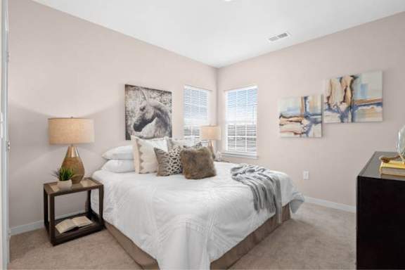 A bedroom with a large bed, a lamp, and two paintings on the wall.