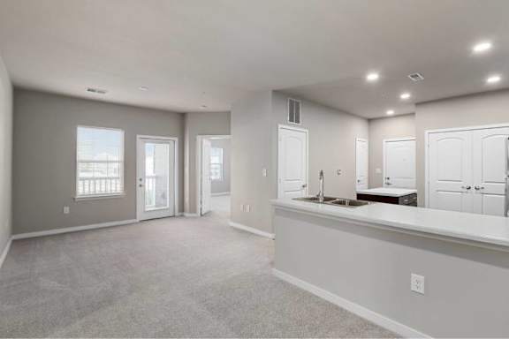 A spacious room with a carpeted floor, a window with a view, and a counter with a sink at Aventura at Wentzville I &amp; II Apartments, Wentzville, MO