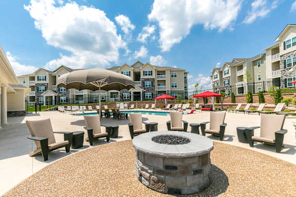 A fire pit sits in the middle of a patio surrounded by chairs and umbrellas.