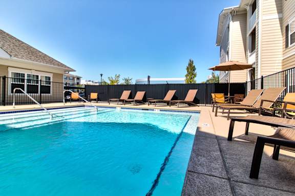 A swimming pool with sun loungers and a building in the background.