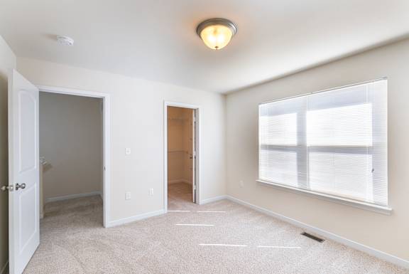 A room with a carpeted floor, a window with blinds, and a ceiling light.