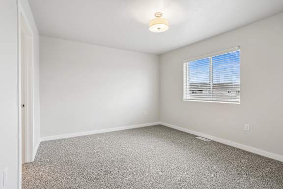 A room with a carpeted floor and a window with blinds.