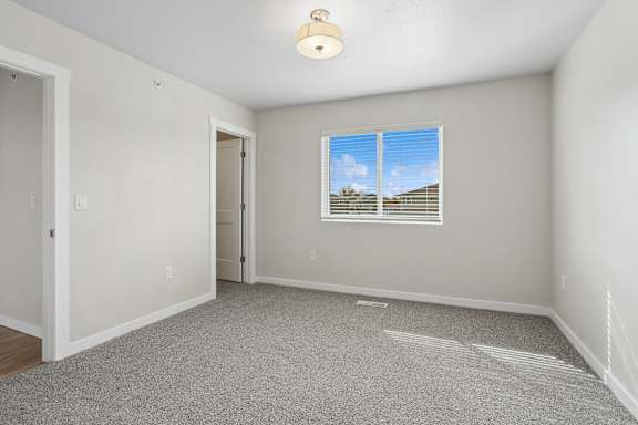 A room with a carpeted floor and a window showing a blue sky with clouds.