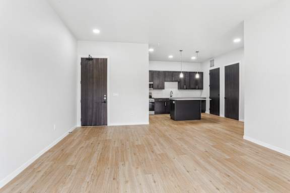 A room with wooden flooring and a kitchen area in the background.