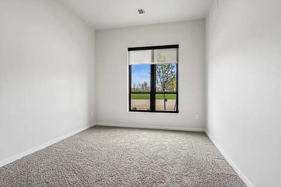 A room with a carpeted floor and a window showing a tree and a road outside.