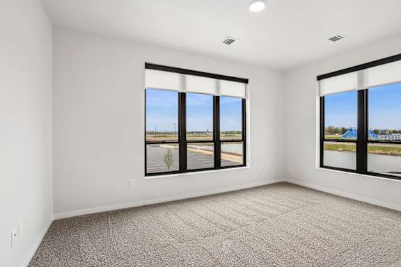 A large empty room with carpeted floor and two large windows.