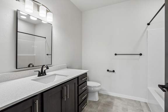 A bathroom with a sink, mirror, toilet and a shower.