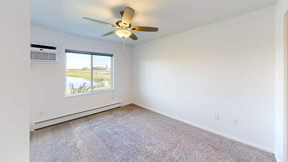 A room with a ceiling fan and a window overlooking a field.