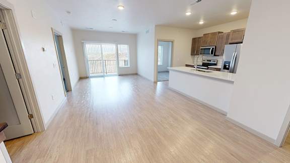 A spacious living room with wooden flooring and a kitchen area with appliances.