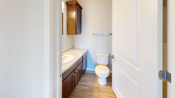 A white toilet sits in a small bathroom with a sink and wooden cabinets.