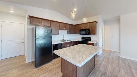 A kitchen with a black fridge and microwave above a counter with a marble top.