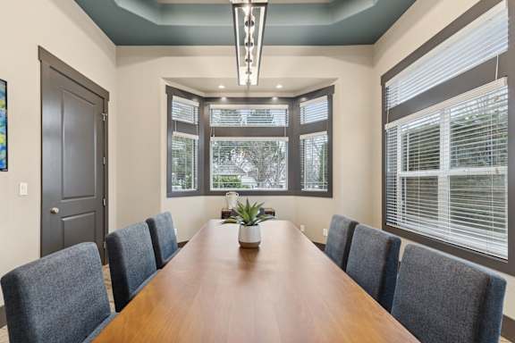 A long brown table is surrounded by grey chairs in a room with a large window.