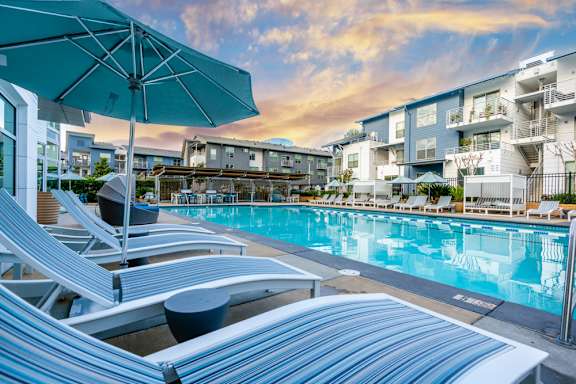 A poolside with sun loungers and a blue umbrella.