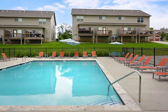 A swimming pool surrounded by red chairs and apartment buildings in the background.